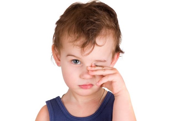 Ребенок с врожденным астигматизмом чешет глаз